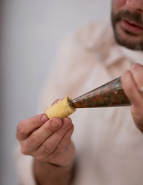 Ein Chefkoch füllt kleine knusprige Röllchen mithilfe eines Spritzbeutels 