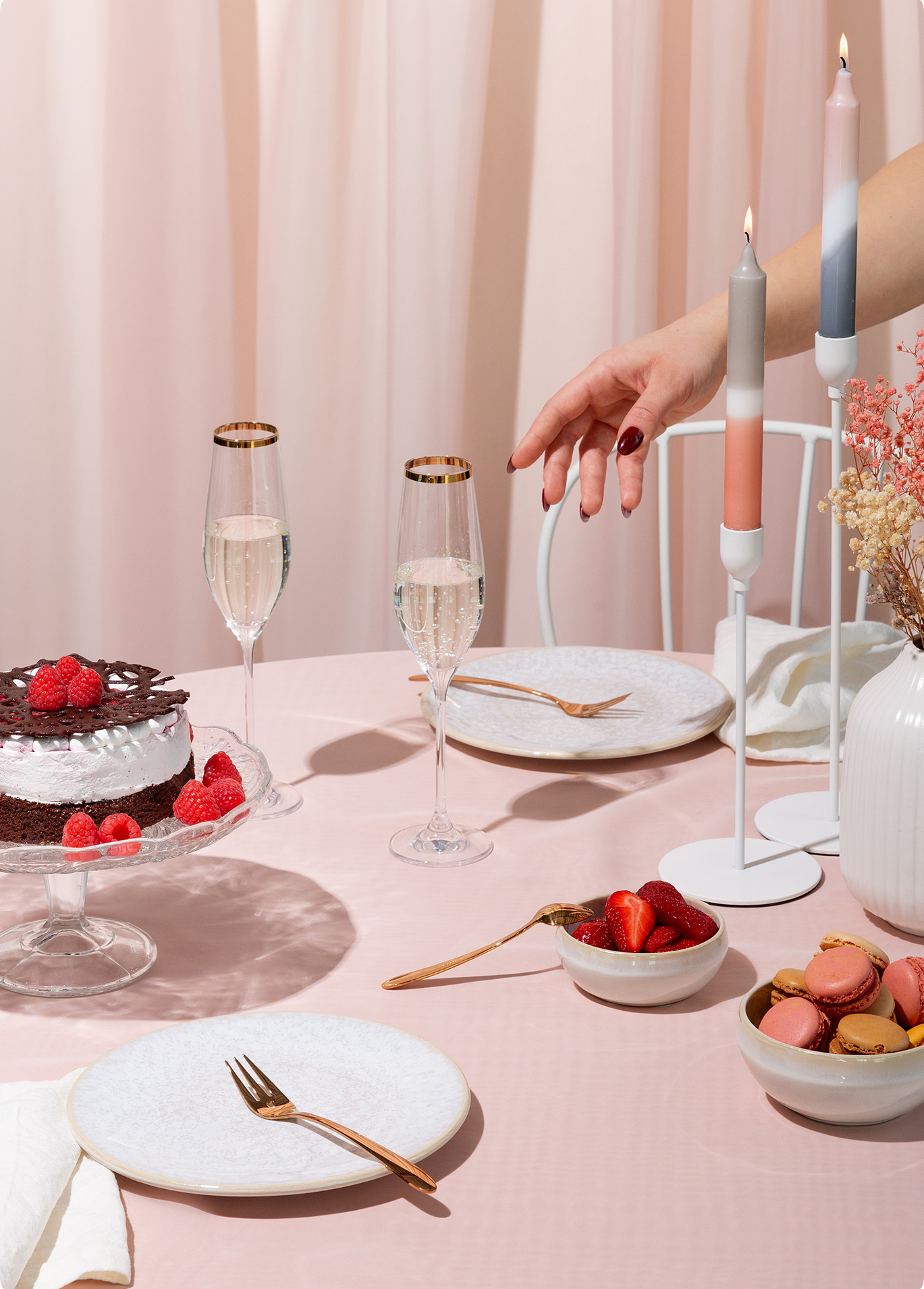 Ein gedeckter Tisch mit Desserts, Gläsern, Kerzen und goldenem Besteck auf einer rosafarbenen Tischdecke 